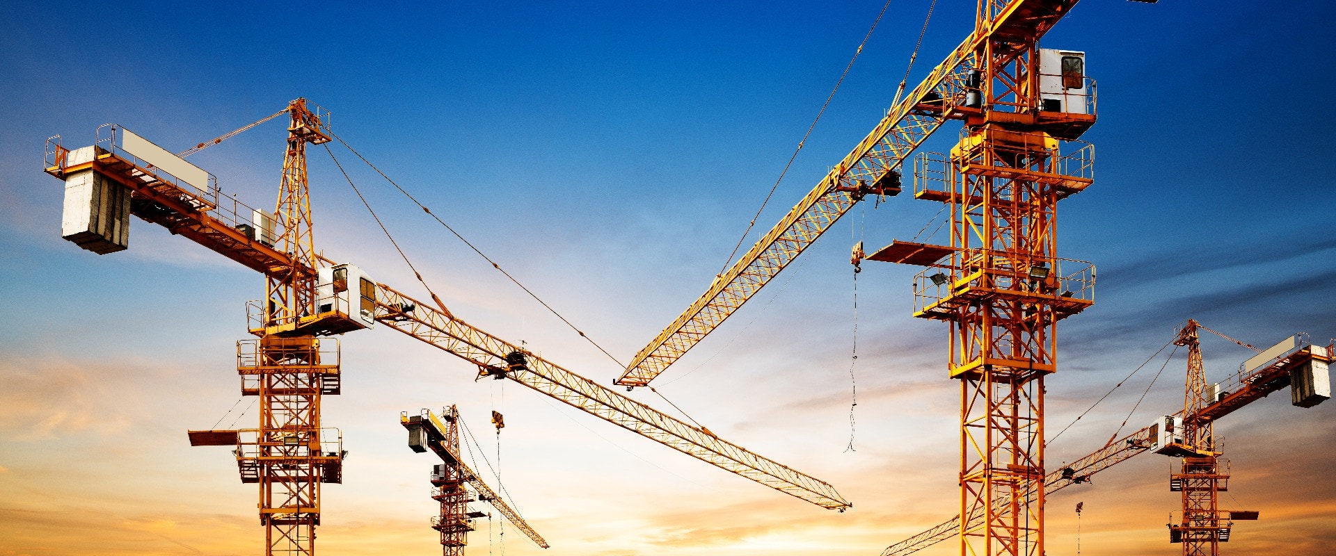 Industrial construction cranes and building silhouettes over sun at sunrise.