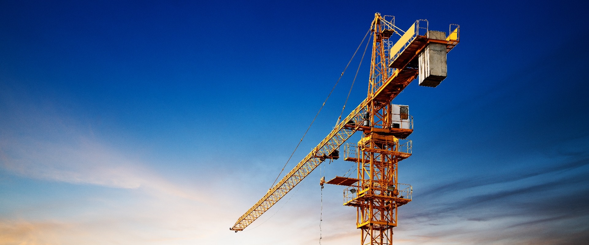 Industrial construction cranes and building silhouettes over sun at sunrise.