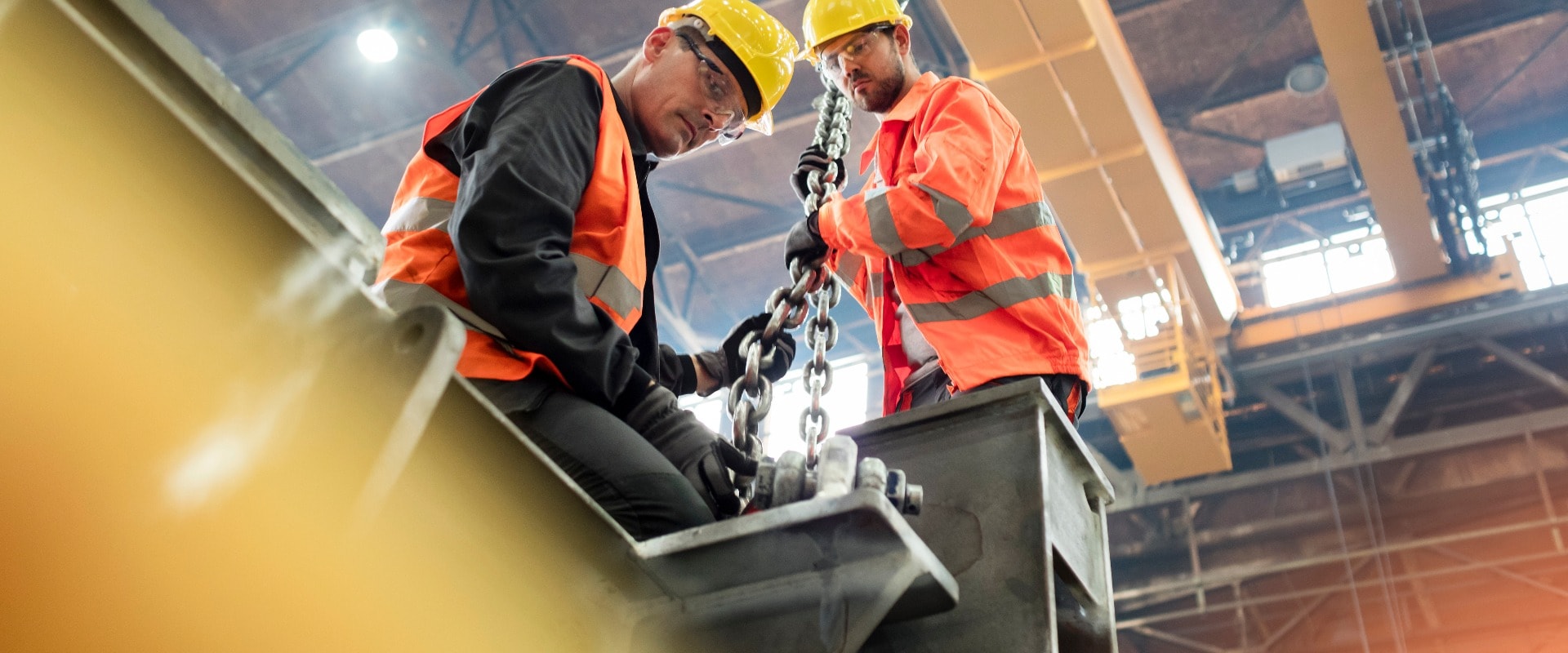 Steel workers fastening steel to crane in factory