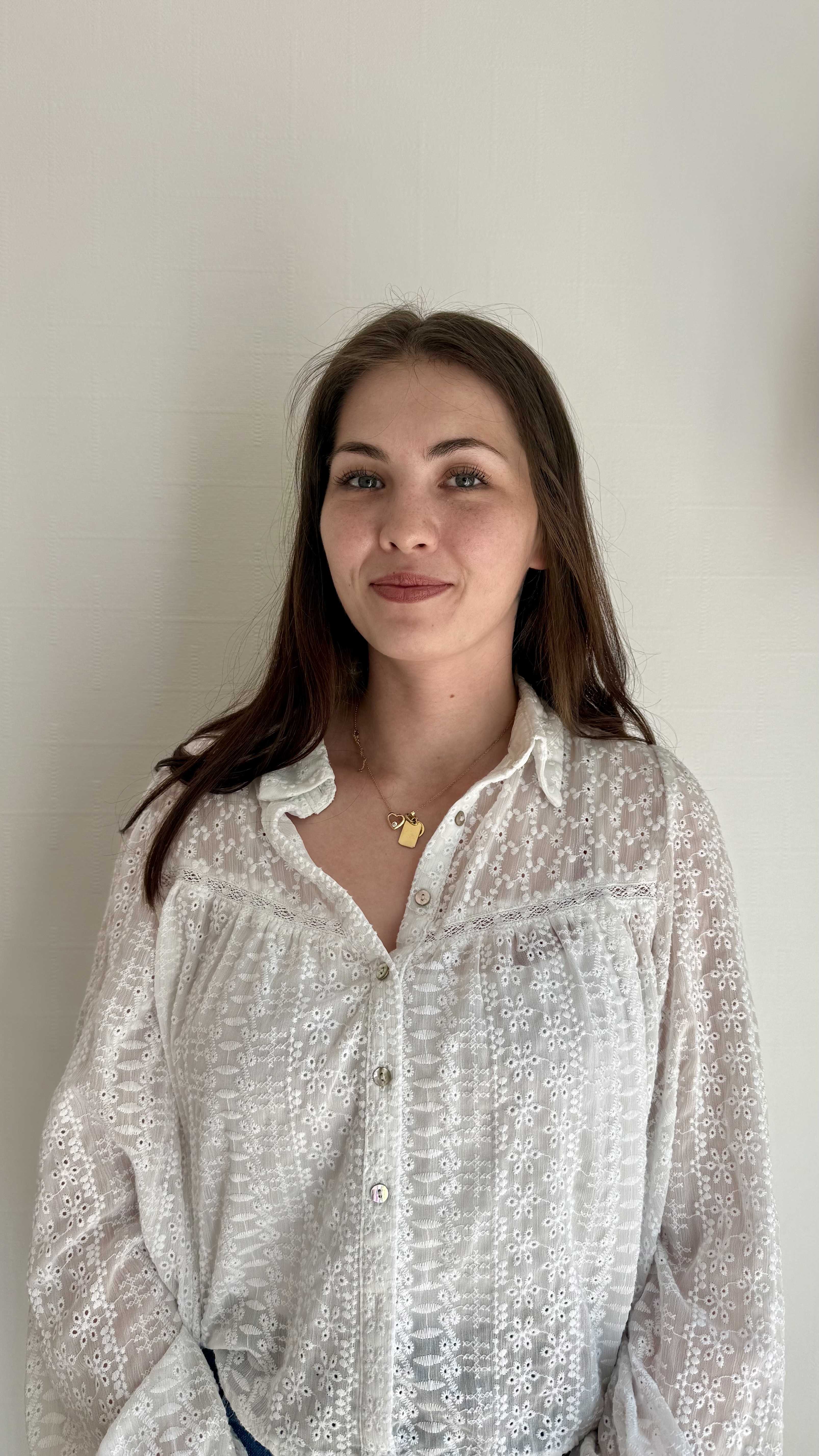 Frau mit neutralem Blick braunen Haaren weißer Bluse goldener Kette